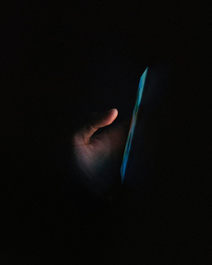 A hand holding a smartphone in the dark, lit by the blue glow of its screen