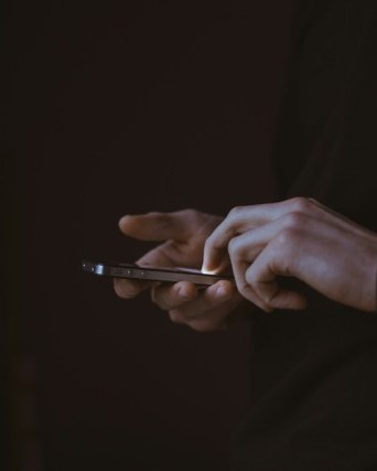 Hands using a smartphone in the dark, its screen lighting the fingers